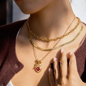 Nahaufnahme dreilagiger Goldketten mit rotem Herzanhänger und eleganter Schlangenkette