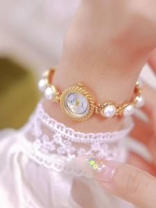 Detail of elegant gold chain watch featuring large pearls and a white dial on wrist