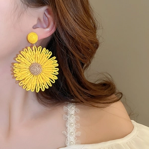 Detail view of woven yellow sunflower tassel earring with rich spiral texture on model
