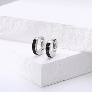 Gros plan de créoles en argent avec zircons carrés noirs sur un socle en pierre blanche