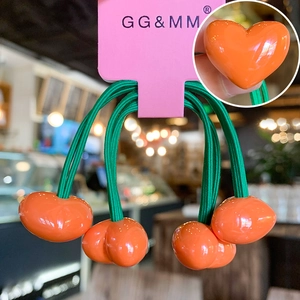 Detail of high-elastic green braided hair ties with glossy orange heart-shaped pendants