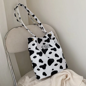 Detail of cow print canvas tote bag featuring metal side snap button and woven brand label