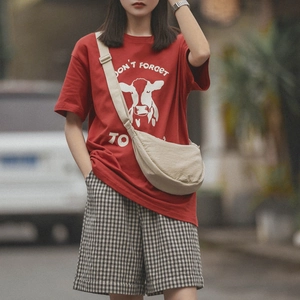 Model wearing a stylish beige crescent bag paired with a red graphic tee and plaid shorts
