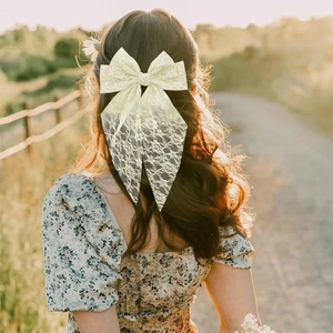 Rear view of a model wearing a large cream lace bow hair clip with long flowing ribbons
