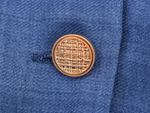 Nahaufnahme eines goldenen Metallknopfes auf einem marineblauen Stoff des Blazer-Kleids