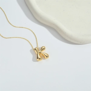 Macro shot of 3D gold letter K pendant on a fine chain over a textured tray