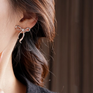 Gros plan de boucles d'oreilles nœud en argent portées par un mannequin sur tissu