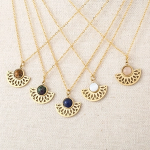 Five bohemian fan-shaped gold necklaces with colorful natural stones on fabric background