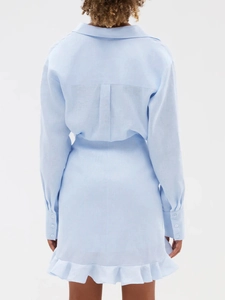 Rear view of light blue linen shirt dress featuring back pleat and ruffled hem detail