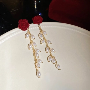 Macro view of red flocked flower earrings with elegant white pearl tassels on ceramic