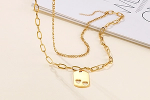 Detail of gold double-layered necklace featuring hollow heart pendant on rectangular plate