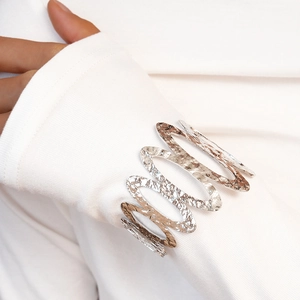 Macro detail of silver hammered metal cuff bracelet with wave texture on white sleeve