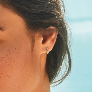 Close-up of a gold-plated hoop earring with turquoise beads worn on a model's ear lobe