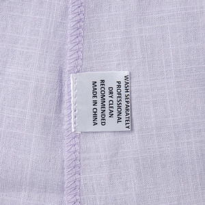 Detailansicht des Pflegeetiketts und der Baumwolltextur auf einem lavendelfarbenen Kleid