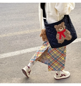 Quilted black tote bag featuring a 3D teddy bear with a red scarf on model in street view