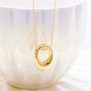 Detail of a gold oval pendant necklace hanging on a white pearl luster porcelain cup