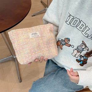 Detail of multi-color tweed makeup bag with woven label held in a cafe setting