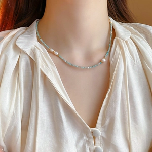 Detailed view of dainty gold-plated geometric pearl necklace with light blue beads on model