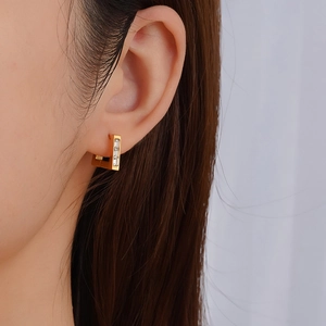 Close-up of gold rectangular hoop earring with three inlaid clear zircon gemstones