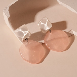 Macro detail of geometric resin earrings with cream diamond and sparkling pink pendants