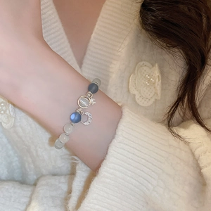 Close-up of cat eye beaded bracelet with silver moon and star charms on a soft wrist