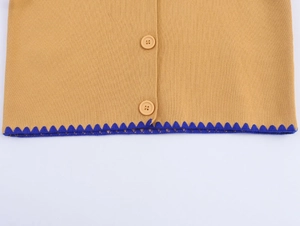 Detailed close-up of yellow knit cardigan hem with blue zigzag trim and round buttons