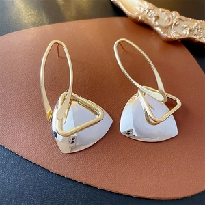 Detail of silver triangle drop earrings with gold hooks on a premium leather surface