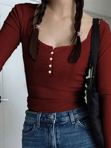 Detail of burgundy long sleeve top with square neck, lace patchwork and white buttons