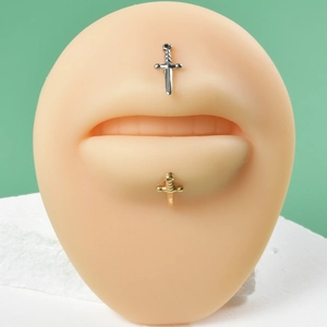 Detail of silver and gold sword-shaped lip piercings displayed on a silicone model