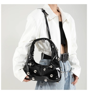 Detail of glossy black patent leather bag with silver punk studs and curved structure