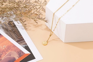 Close-up of golden stainless steel necklace with vintage coin pendant on white prop