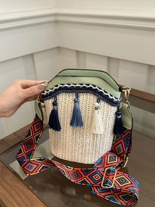 Detail view of woven straw bucket bag with green PU trim and colorful geometric strap