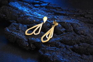 Close-up of golden hollow teardrop earrings displayed on natural dark charcoal base