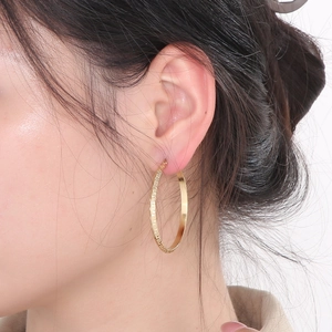 Detail of gold-plated stainless steel hoop earrings with Greek key pattern on a model