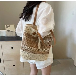 Detail of hollow woven tote bag featuring brown shoulder straps and side tassel charm