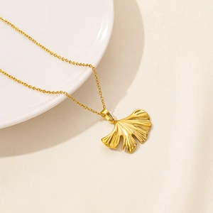 Detail of 18K gold ginkgo leaf pendant with fine texture on a white ceramic plate