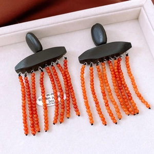 Detail view of ethnic wood geometric earrings with orange red beaded tassels