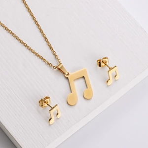 Polished gold music note necklace and stud earrings set on a minimalist white stand