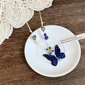 Macro view of blue ceramic butterfly pendant with woven cord on vintage wooden surface