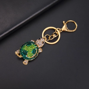 Macro shot of a golden turtle keychain featuring vibrant green and white rhinestones