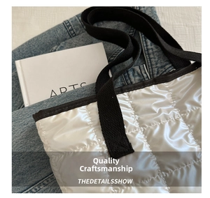 Detail of silver quilted tote bag with metallic finish and black woven strap accents