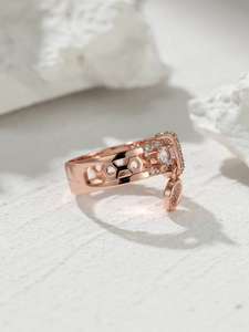 Macro detail of rose gold ring featuring hexagonal cutouts and a small round pendant
