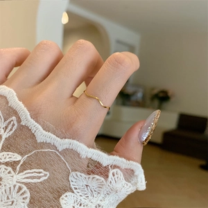 Minimalist gold wavy stacking ring worn on finger with soft aesthetic indoor background
