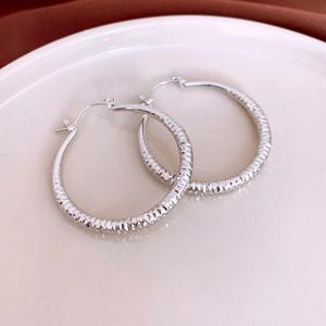 Macro shot of silver textured hoop earring with diamond-cut pattern on white ceramic