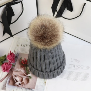 Detailansicht einer grauen Strickmütze mit großem Kunstfellbommel in Geschenk-Deko