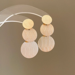 Detail view of triple-layered circular gold earrings with brushed metallic texture