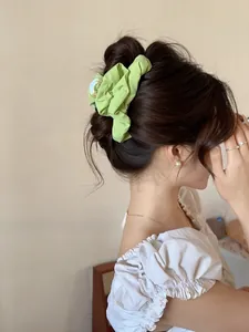 Detail of light green pleated fabric scrunchie styled in a bun with pearl earrings