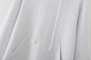 Detail of light grey hoodie featuring front pocket, adjustable drawstrings and knit texture