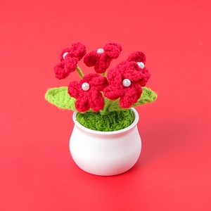 Close-up of handmade red crochet flowers with pearl centers in a white ceramic pot