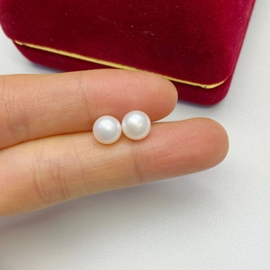 Close-up of round white freshwater pearl earrings on finger showing real size